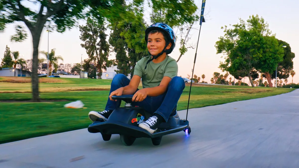 Boy wearing a helmet rides the Razor Crazy Cart Shift Lightshow at speed along a smooth park path at dusk