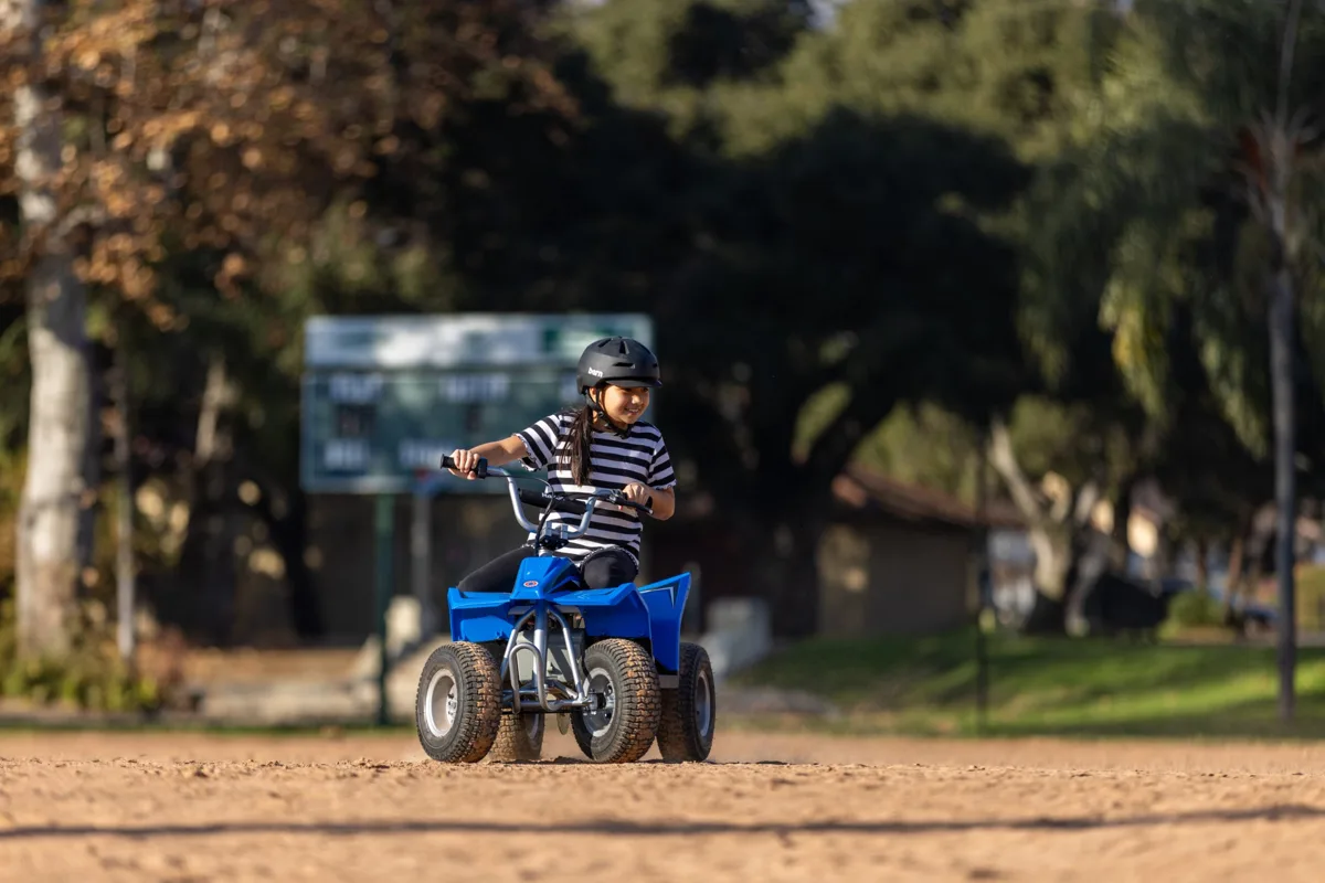Razor Dirt Quad 24V Blue ridden across sandy open ground, showing four-wheel stance, adjustable riser handlebars and blue bodywork