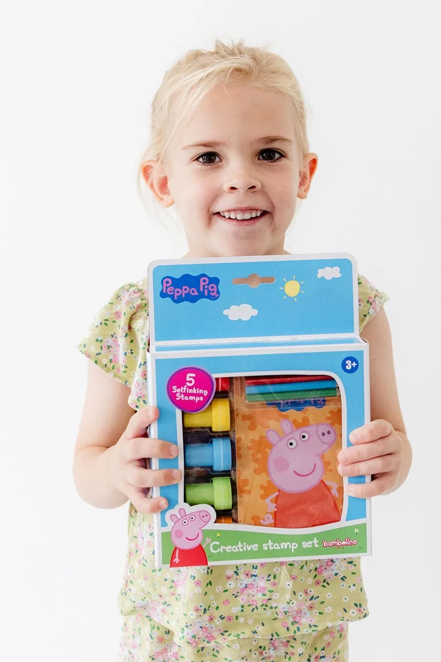 Young child holding open Peppa Pig Creative Stamp Set box displaying five character stamps, coloured pencils and notepad inside
