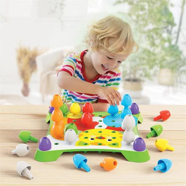 Toddler smiling while stacking large colourful Quercetti Jumbo Peggy Evo pegs on the green pegboard, ages 2 plus
