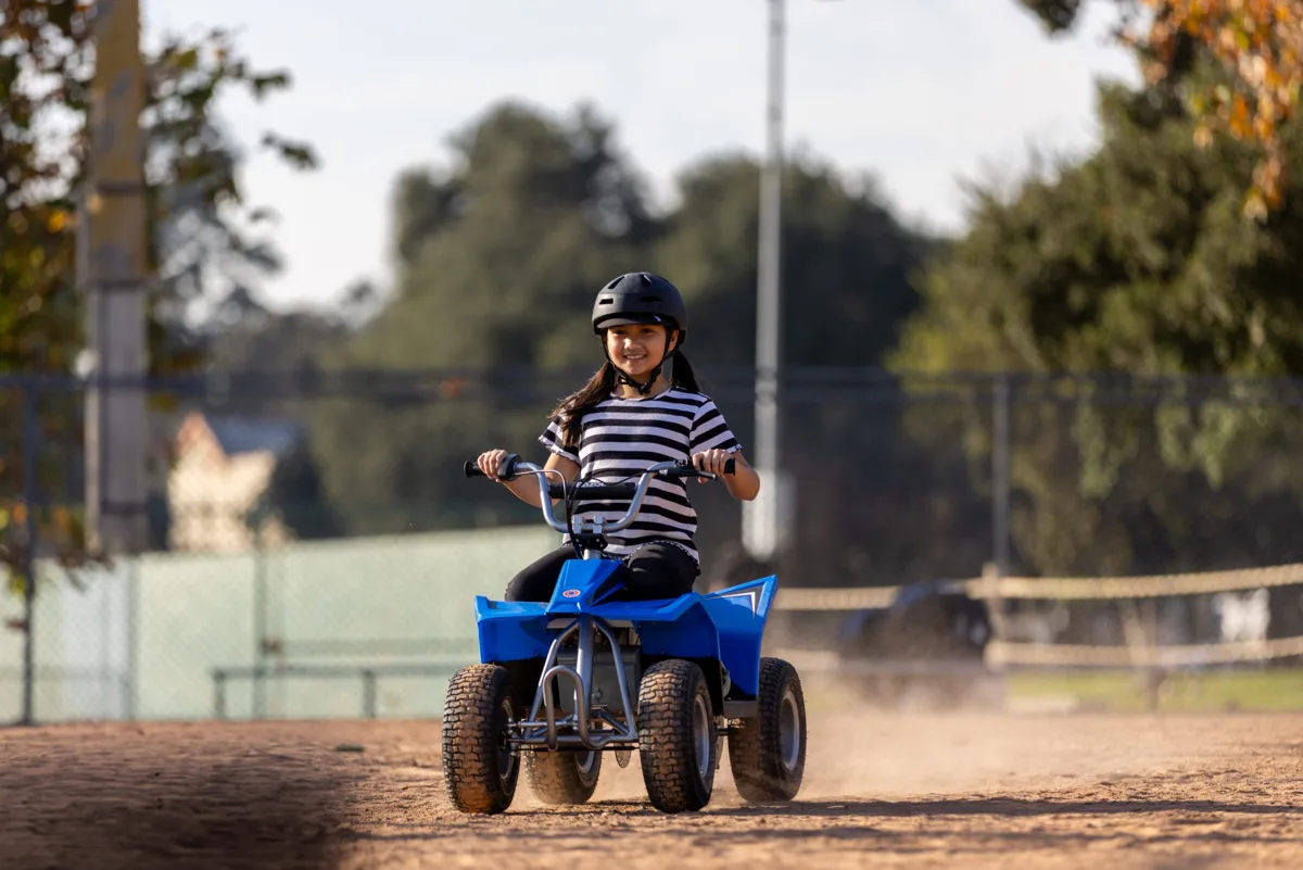 Razor Dirt Quad 24V Blue ridden at speed on a dirt surface, showing rear suspension and pneumatic knobby tyres kicking up dust
