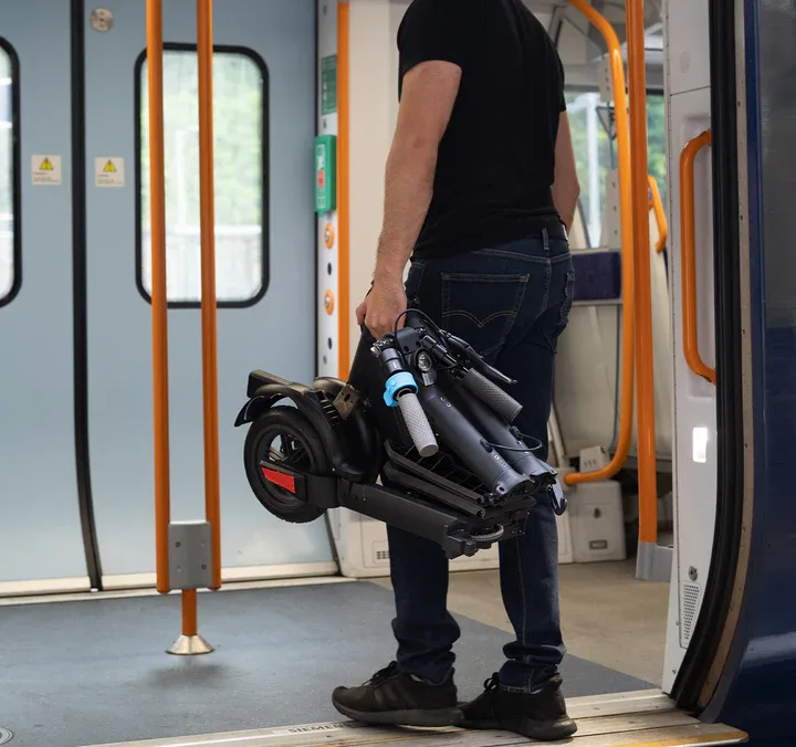 Man holding folded Riley RS3 electric scooter on public transport, demonstrating ultra-compact size and portability