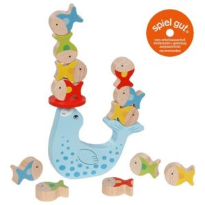The Goki wooden balancing game, shaped like a seal, successfully balancing stacks of colourful wooden fish on its nose and tail, with the "Spiel Gut" award logo.