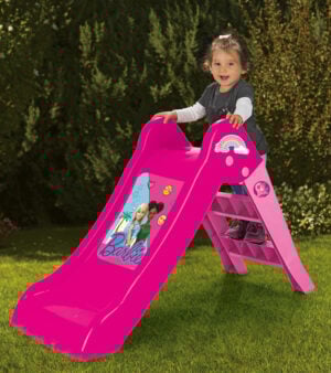 Toddler smiling at the top of a bright pink Barbie toddler slide in a sunny garden.