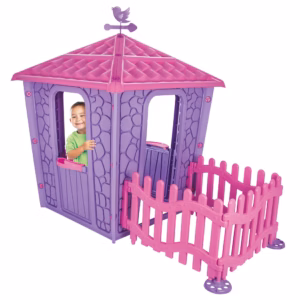 A smiling child playing inside the purple stone house, looking out through the open window above the pink fence.
